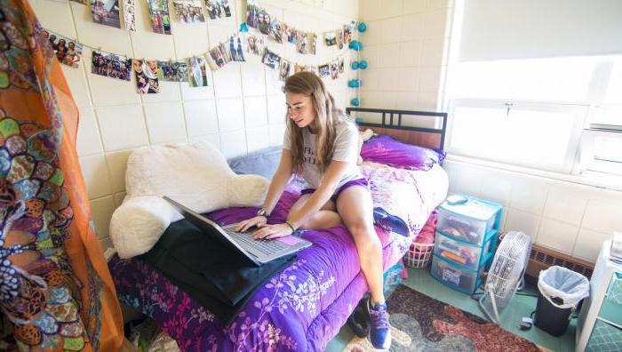 一位年轻的十大赌博靠谱信誉网站的女学生坐在宿舍的床上，一边用笔记本电脑工作.
